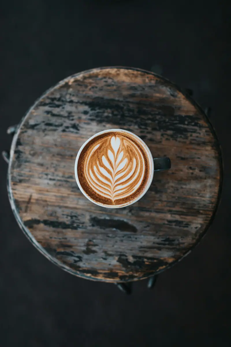 Cappuccino mit Rosetta in der Crema, von oben auf einem alten Holzhocker