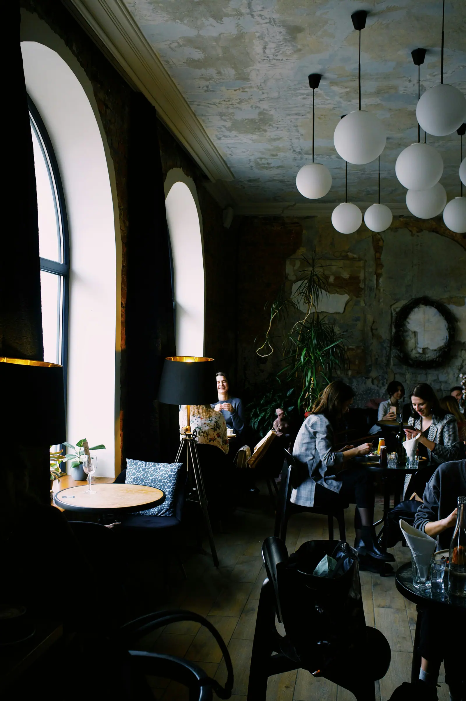 Gäste bei Kaffee und Gesprächen unter Kugellampen, alte Putzwände und hohe Bogenfenster